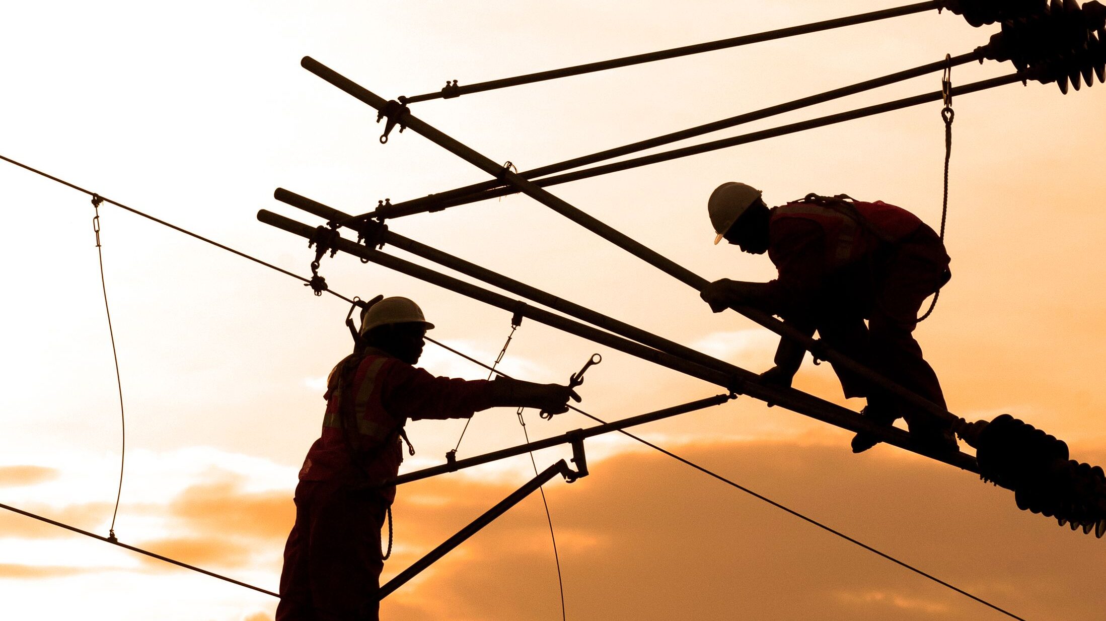 Electrical workers repairing power lines at sunset